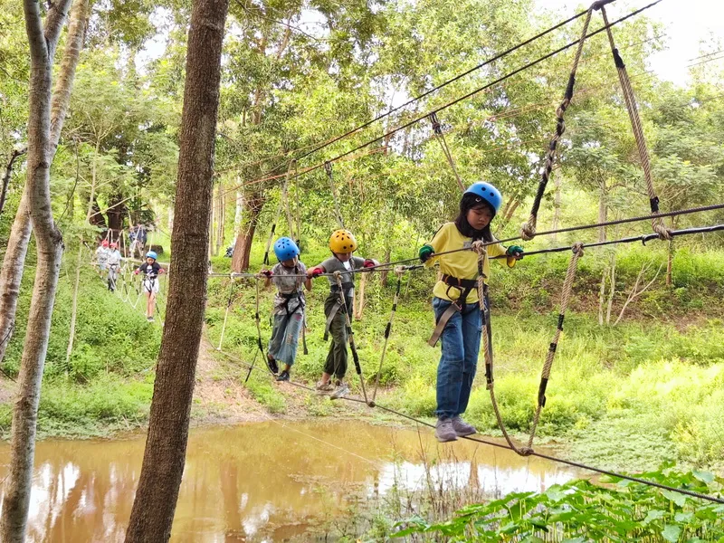 น้อง ๆ สวมหมวกนิรภัยเดินสะพานเชือกข้ามน้ำในฐานผจญภัย ผึ้งหลวง แคมป์กราวด์