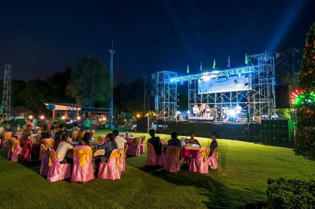 งานเลี้ยงหมู่คณะกลางแจ้งยามค่ำ โต๊ะจัดเลี้ยงพร้อมเวทีคอนเสิร์ตดนตรีสด